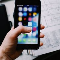 A hand holding a smartphone with an app icon visible on screen