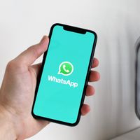A hand holding a smartphone showing the WhatsApp app
