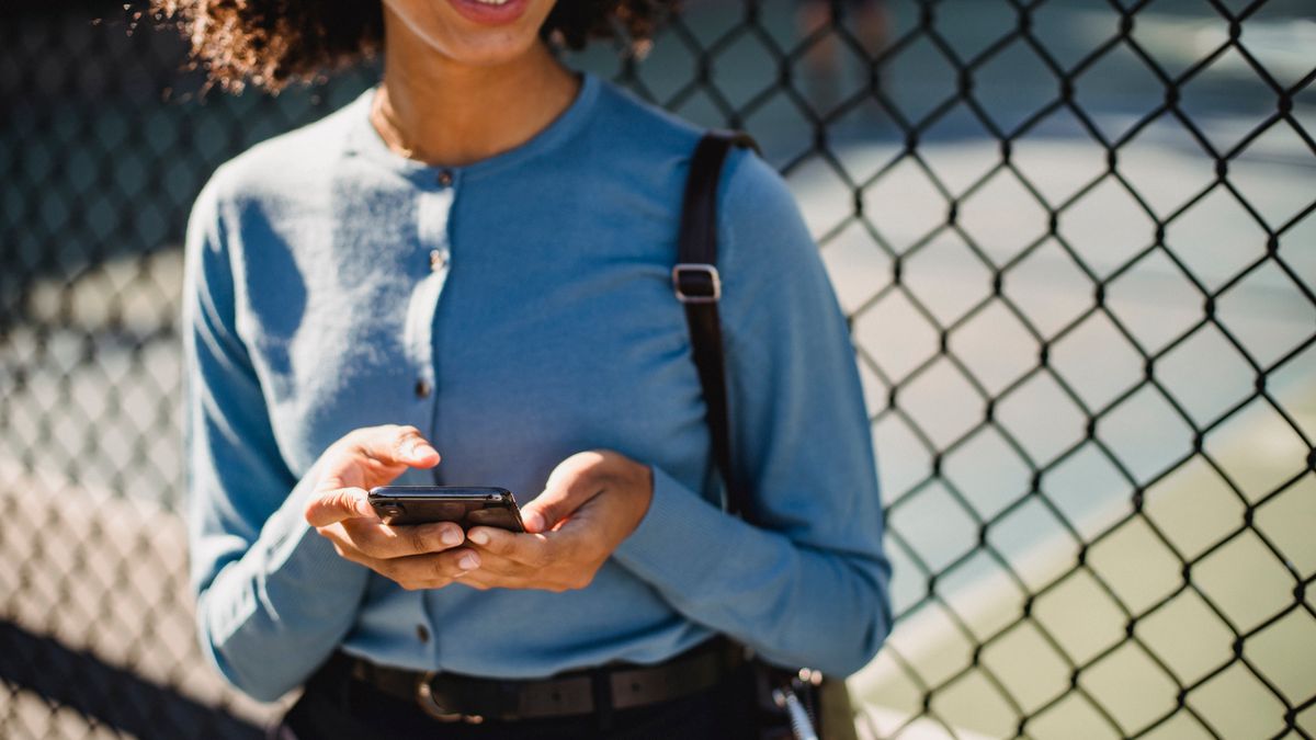 Woman smiling while using a smartphone outdoors, registering for a casino account