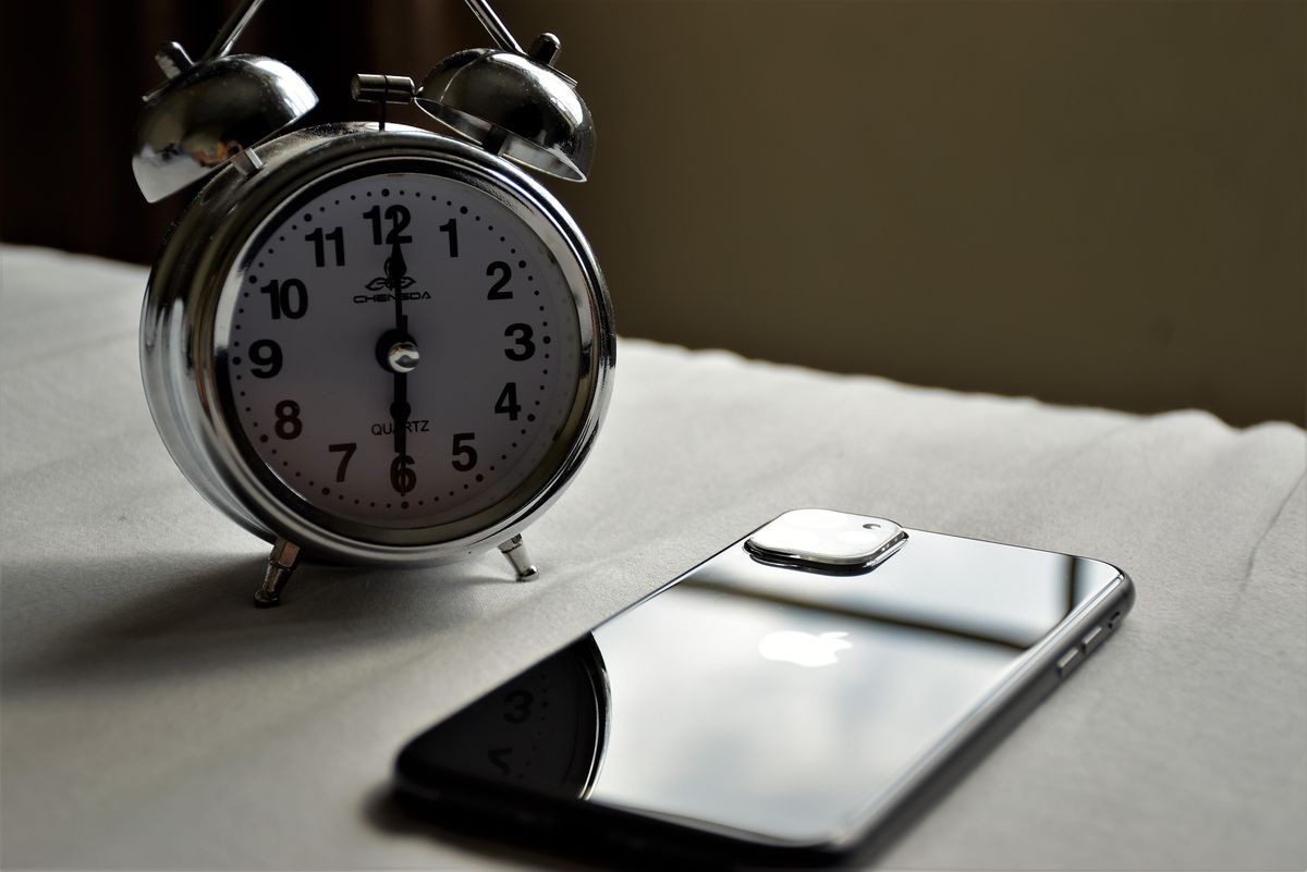 A silver alarm clock and a smartphone side by side on a light surface, representing timing a withdrawal