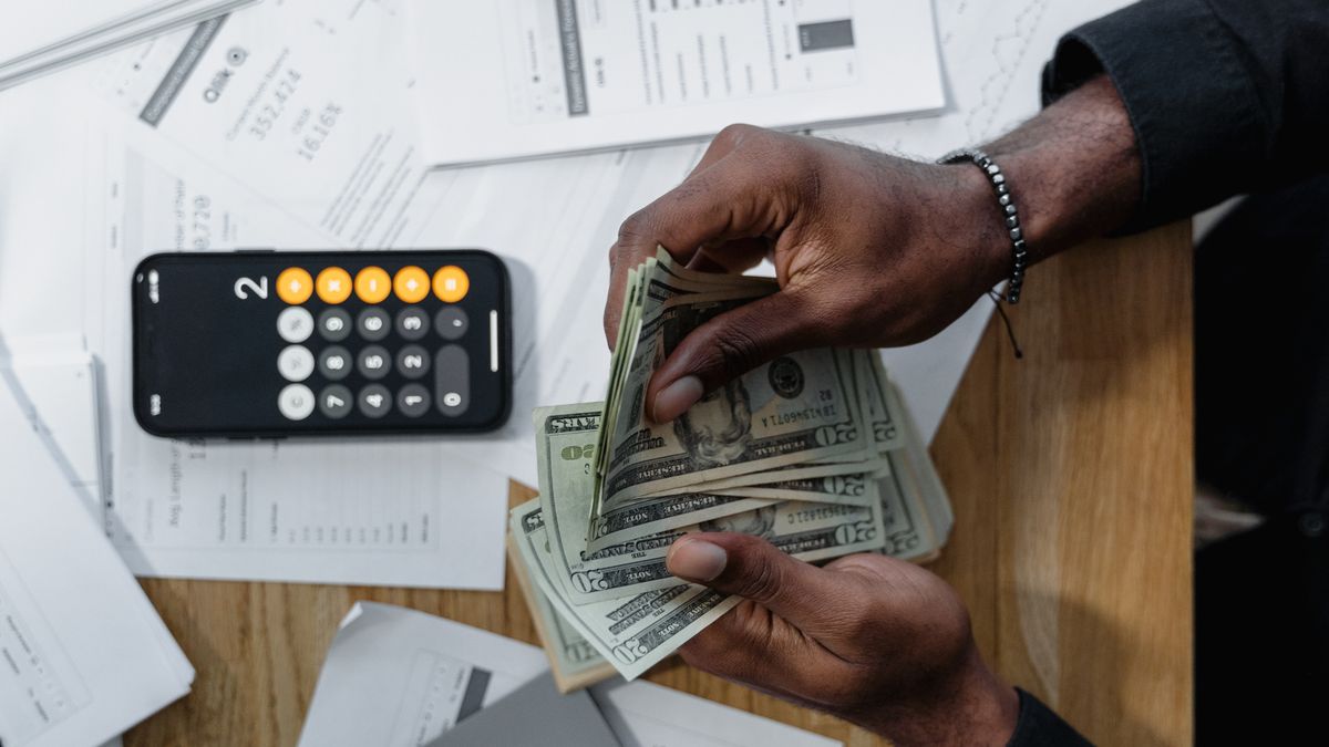 Person counting cash over documents with a smartphone calculator, checking a withdrawal amount