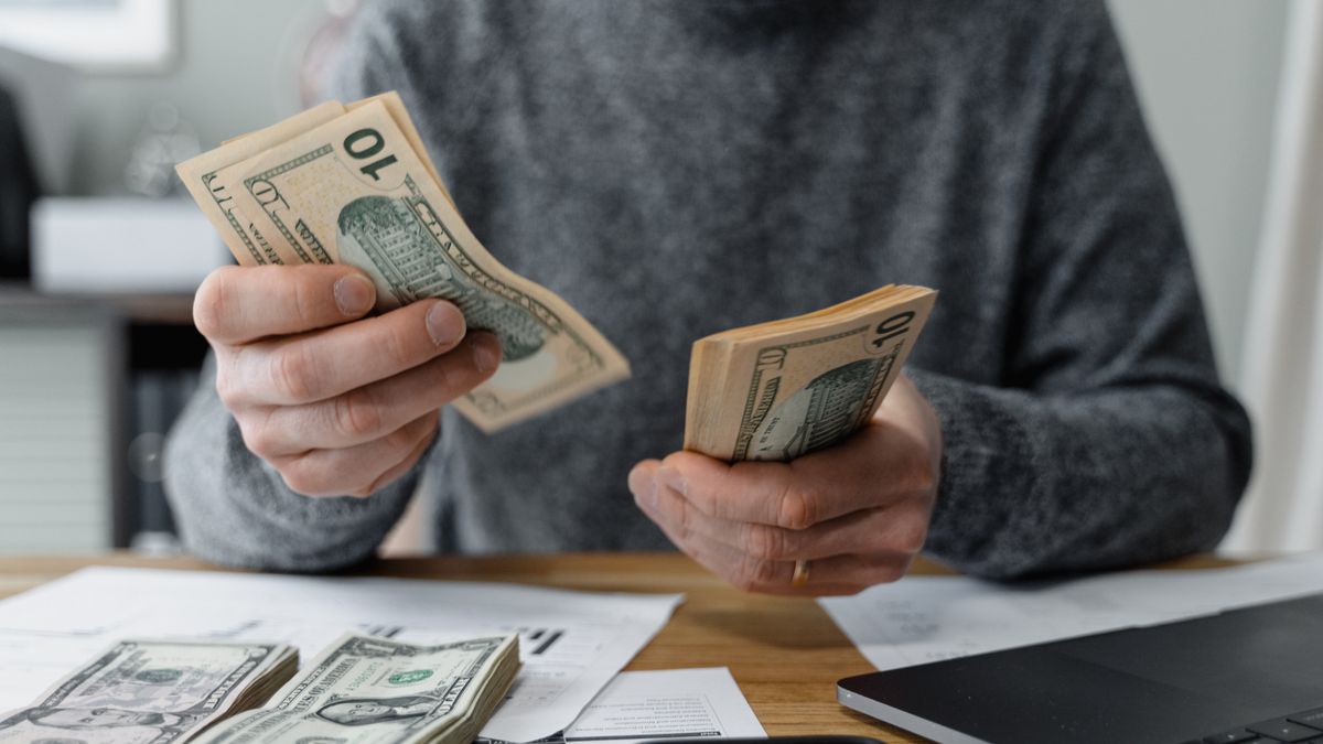 Close-up of a person counting cash with a calculator and paperwork on a desk