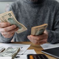 Hands counting cash beside a calculator and paperwork