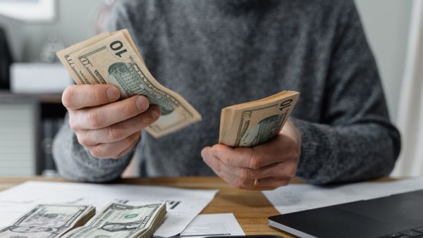 Close-up of a person counting cash with a calculator and paperwork on a desk