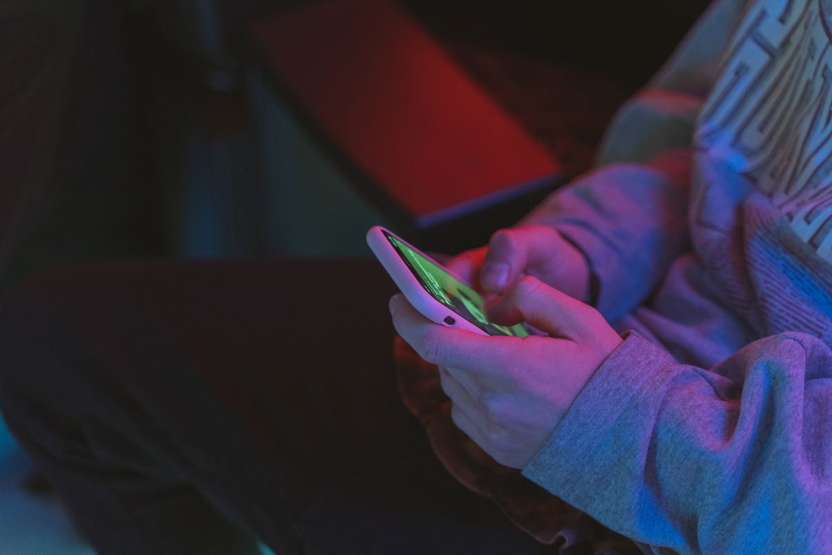 Close-up of hands holding a smartphone in a dimly lit indoor setting with neon lighting