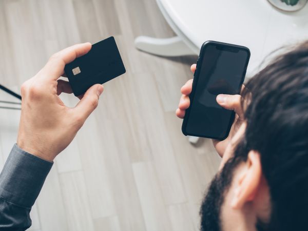 Close-up of a man holding a smartphone and card while making an online payment