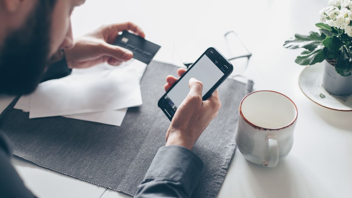 Man using a smartphone and card to complete an online payment, similar to a Kundu365 bank transfer deposit
